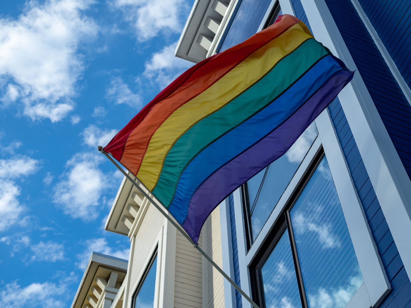 Upward view of gay pride, LGBT flag handing outside of a house.