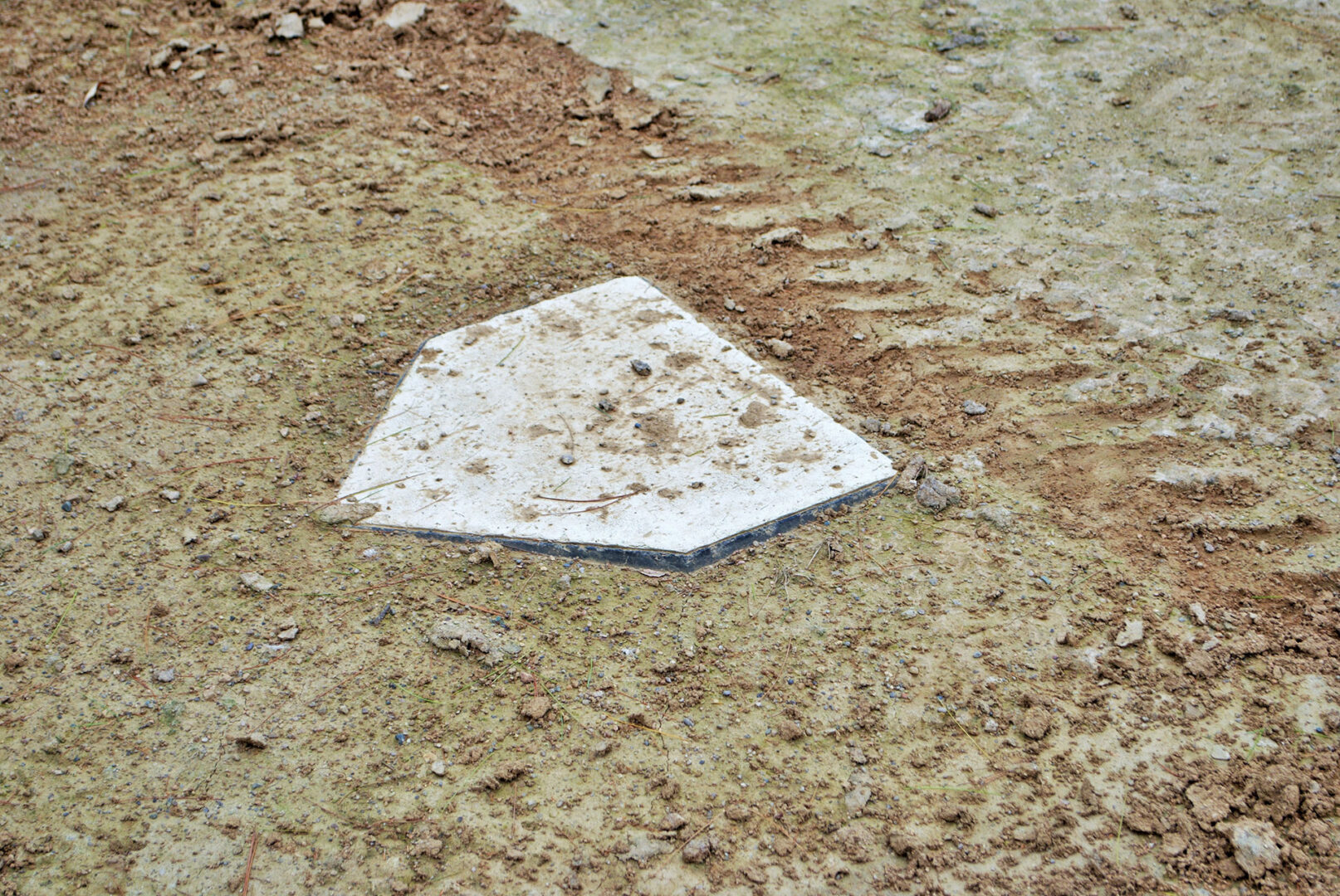 Dirt covered home plate from a deserted baseball diamond.