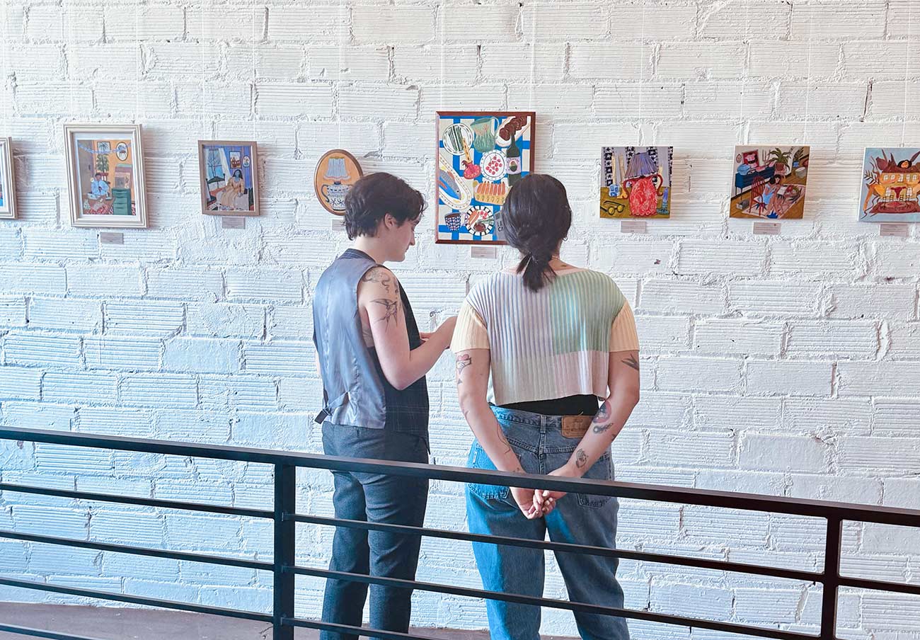 Two young women looking at pieces of artwork at Queermunity.