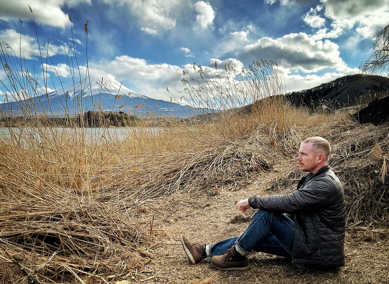 Travel writer Mikey Rox sitting in a filed with a large mountain in the distance.
