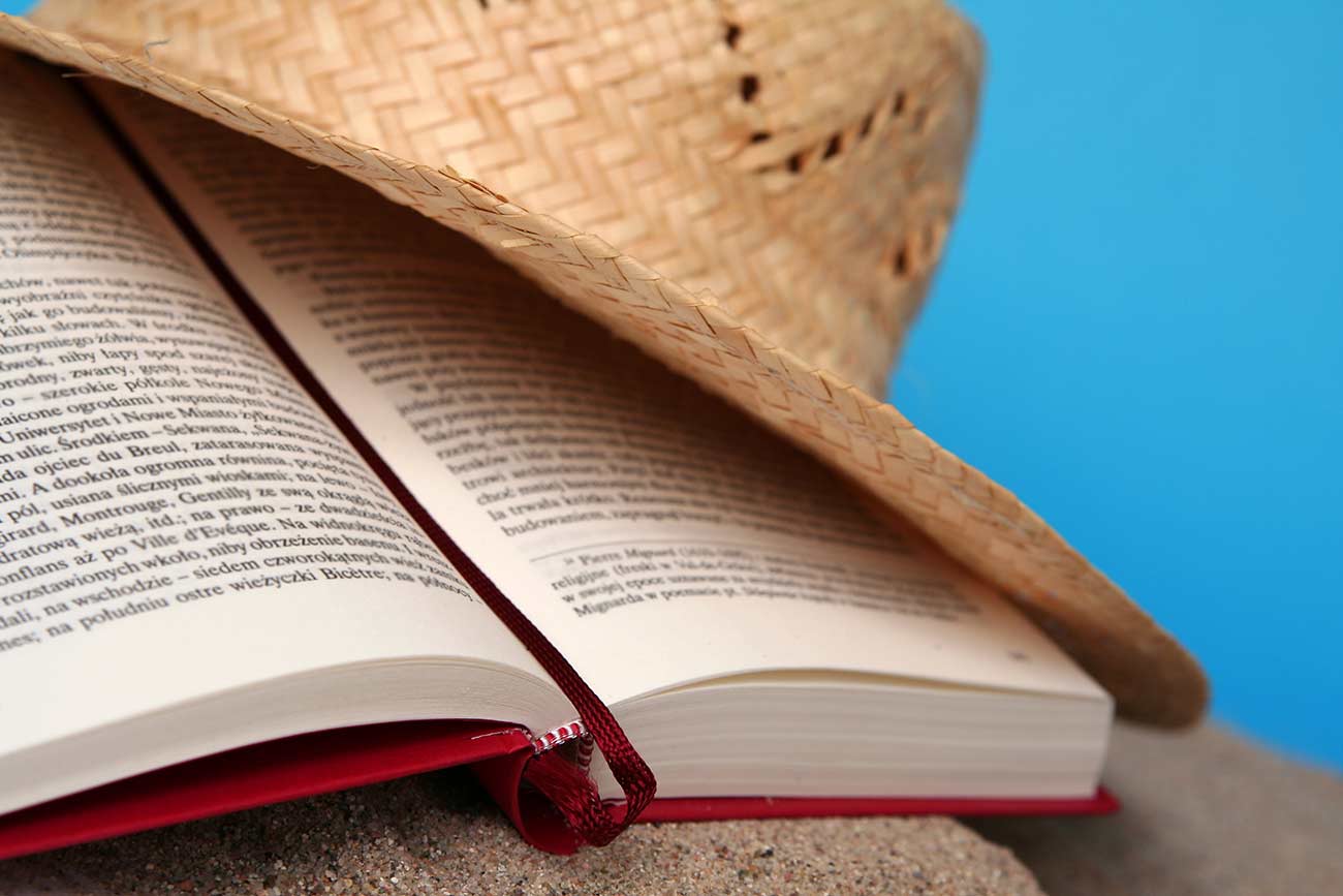 Opened book on a sand with summer hat.
