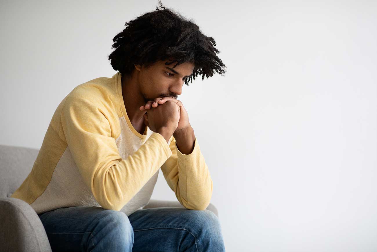 Thoughtful Young Black Man Sitting In Armchair