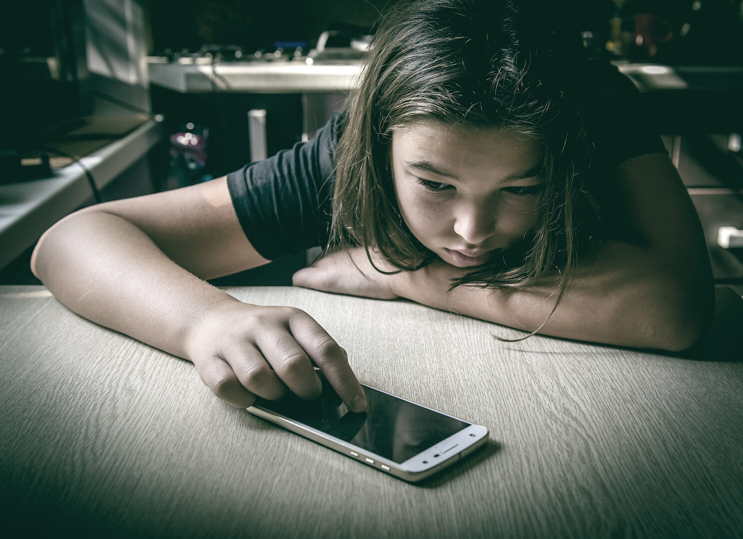 Sad, depressed teenage girl looking at her cell phone.