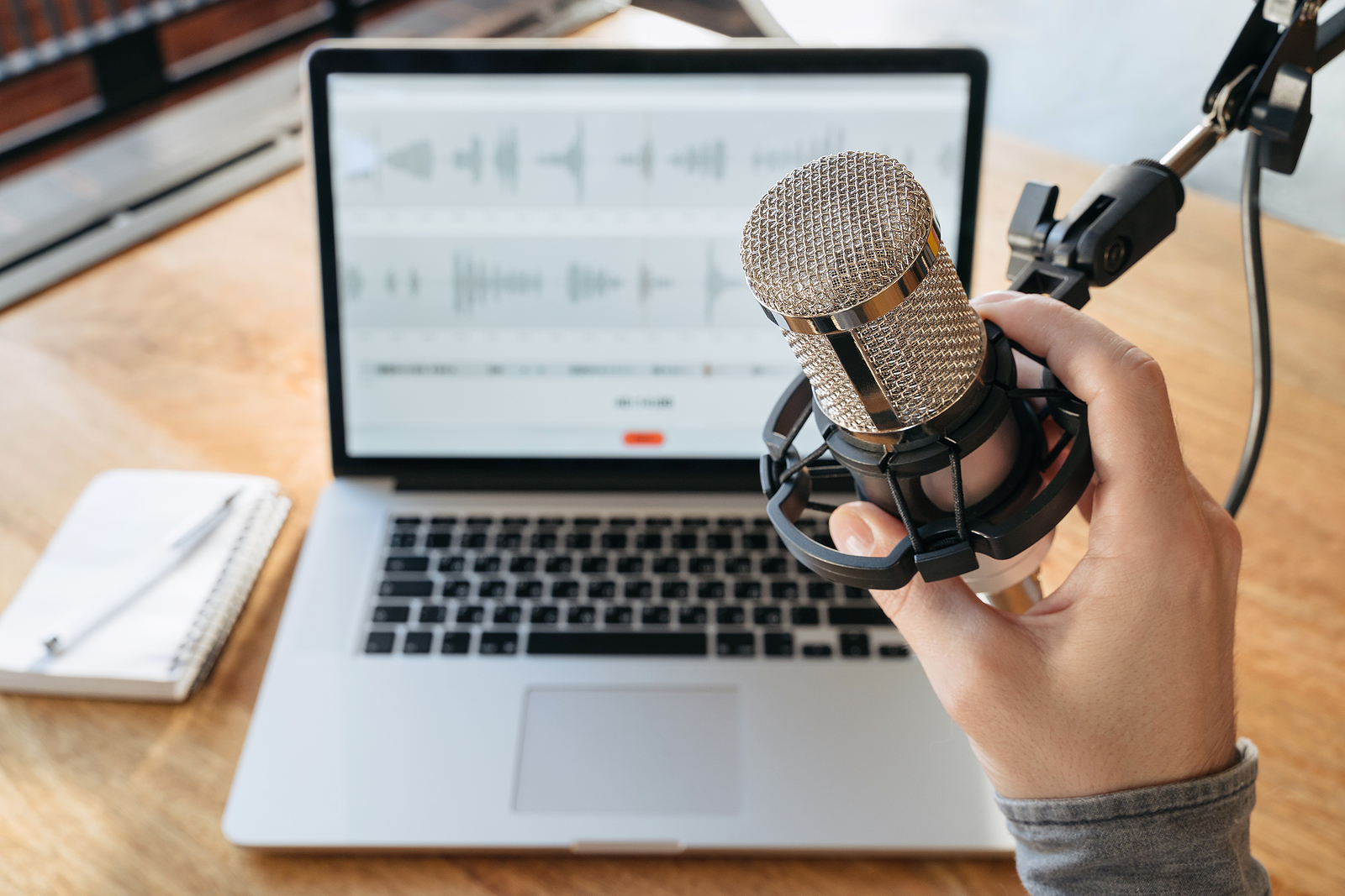 Hand holding a microphone in front of laptop while recording a podcast.