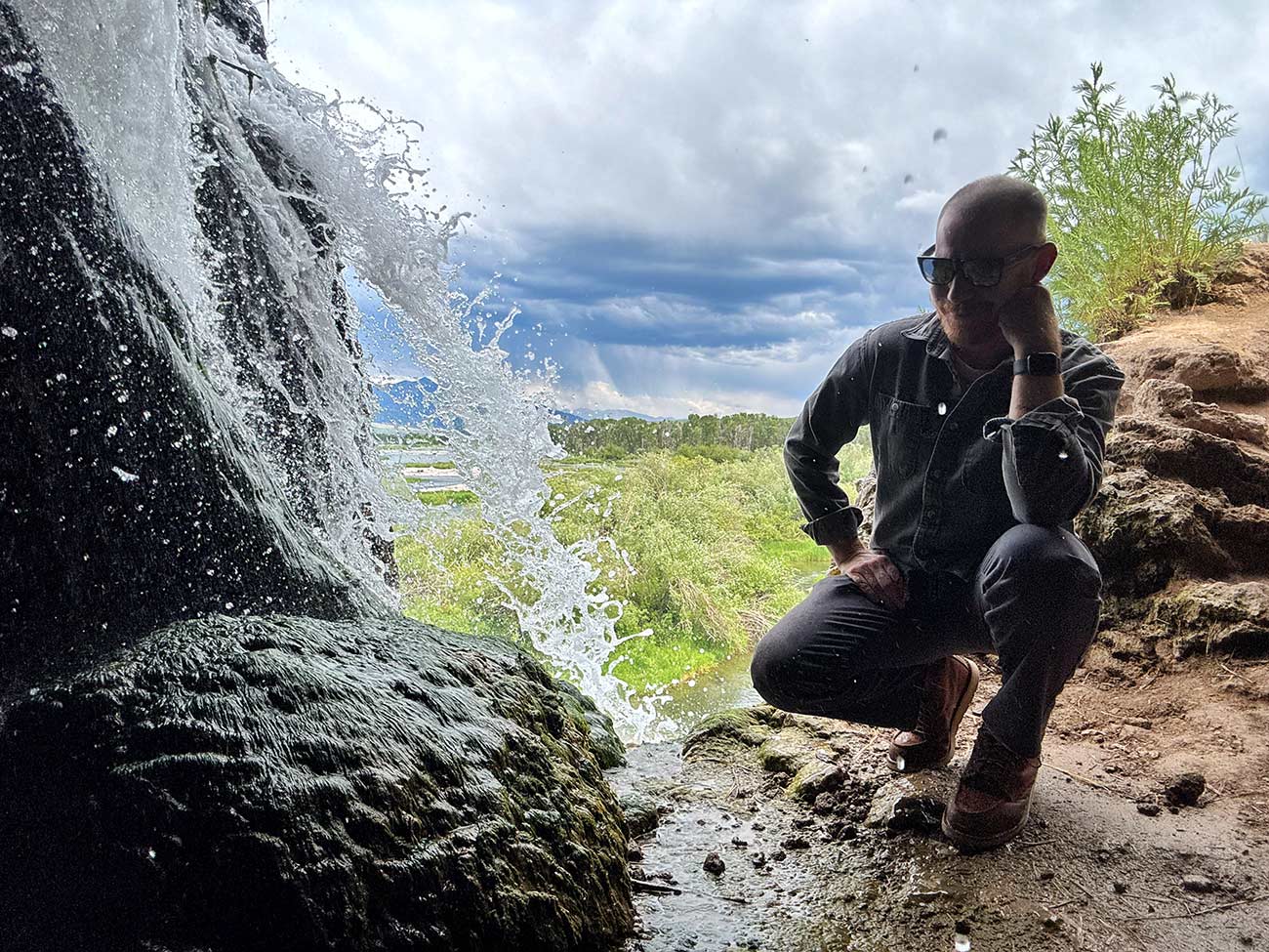 Mikey kneels next to a small trickling water off rocks.