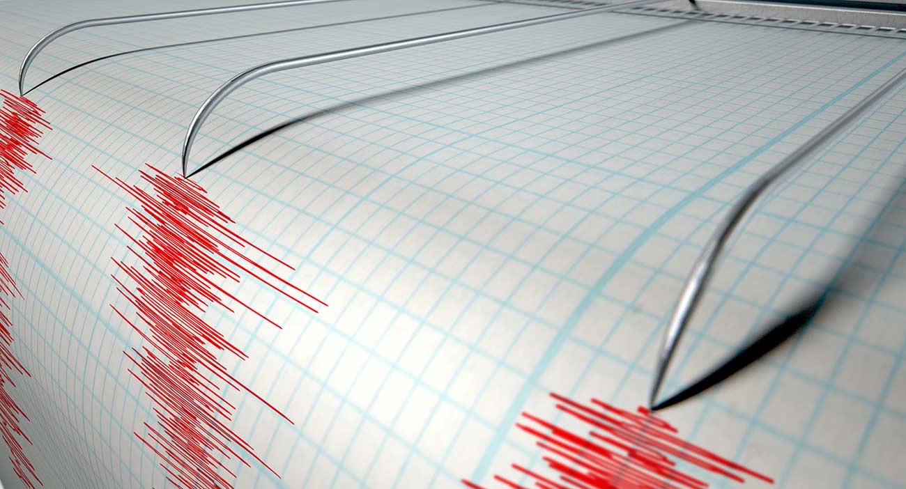 A closeup of a seismograph machine needle drawing a red line on graph paper.